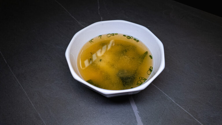 White bowl of miso soup with seaweed and green onions, served at Sushi Station in Westfield, Indiana.