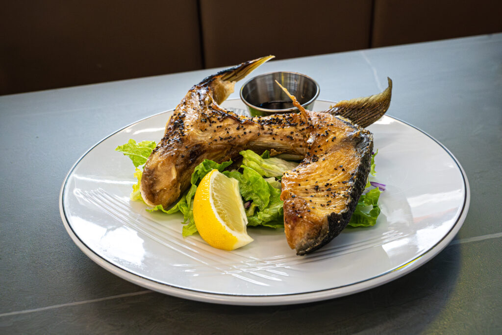 Grilled fish with lemon wedge and greens on white plate at Sushi Station revolving sushi bar in Westfield, Indiana.